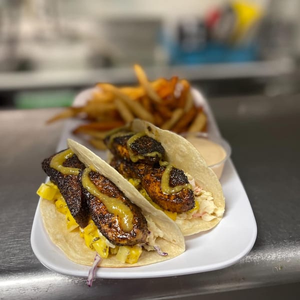 Two Papa Nalu Aloha Grill fish tacos with mango salsa, slaw, and sauce, served with fries.