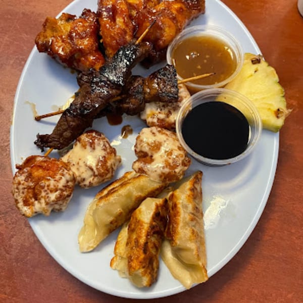 A plate of Hawaiian appetizers including chicken wings, beef skewers, dumplings, and pineapple.