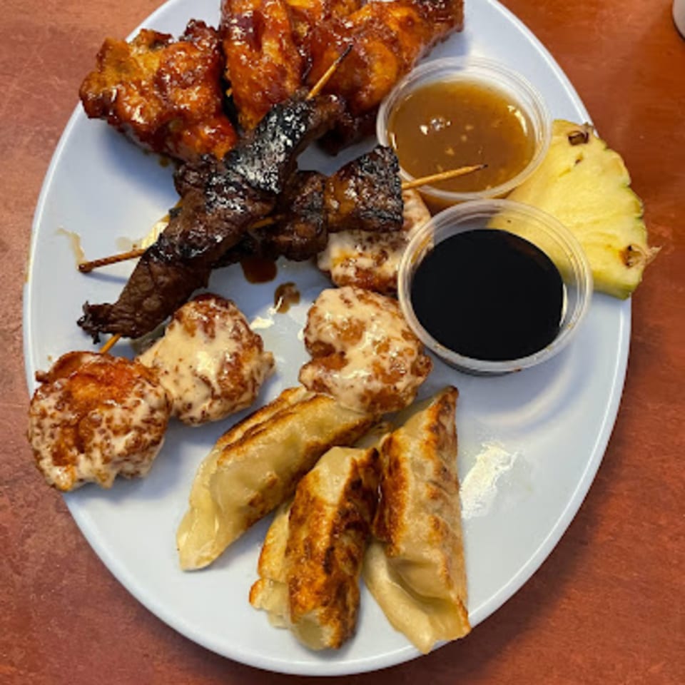 A plate of Hawaiian appetizers including chicken wings, beef skewers, dumplings, and pineapple.