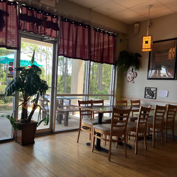 Interior of Papa Nalu Aloha Grill with wooden tables and chairs, large windows, and a potted plant.